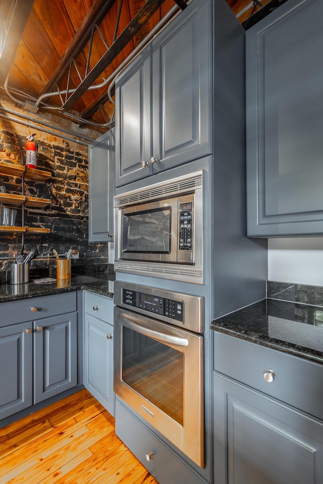 kitchen featuring light wood-style flooring, gray cabinets, stainless steel appliances, and dark stone countertops