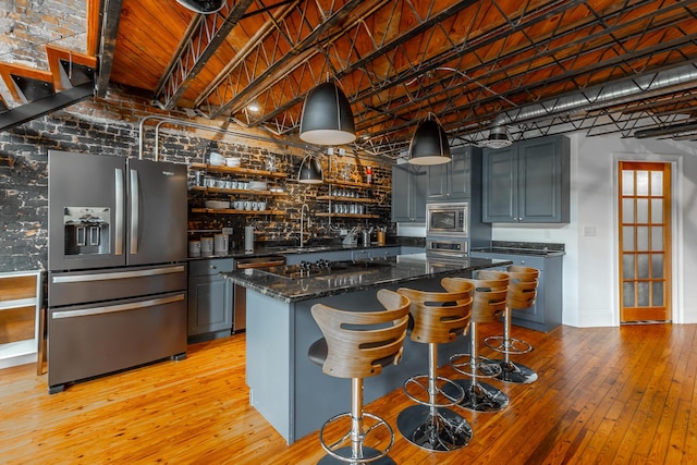 kitchen featuring a center island, light wood finished floors, stainless steel appliances, a sink, and dark stone counters