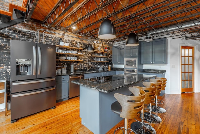 kitchen with stainless steel appliances, a sink, light wood-style floors, a center island, and dark stone countertops