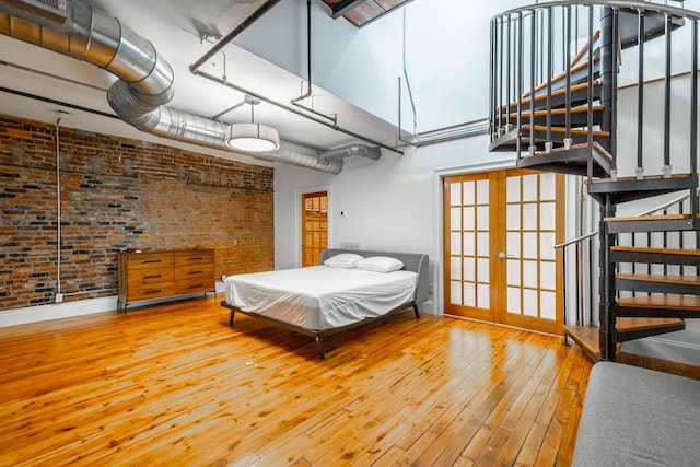 bedroom featuring brick wall, a high ceiling, and hardwood / wood-style flooring