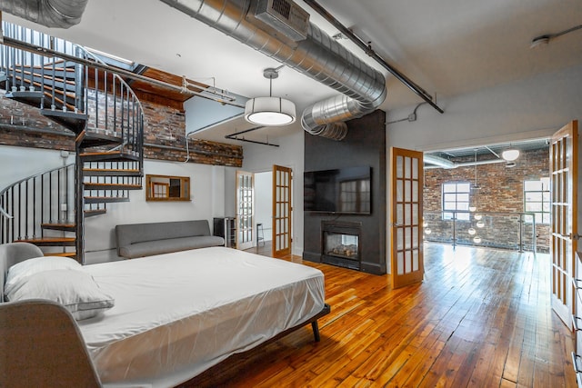 bedroom with a towering ceiling, brick wall, wood-type flooring, french doors, and a multi sided fireplace