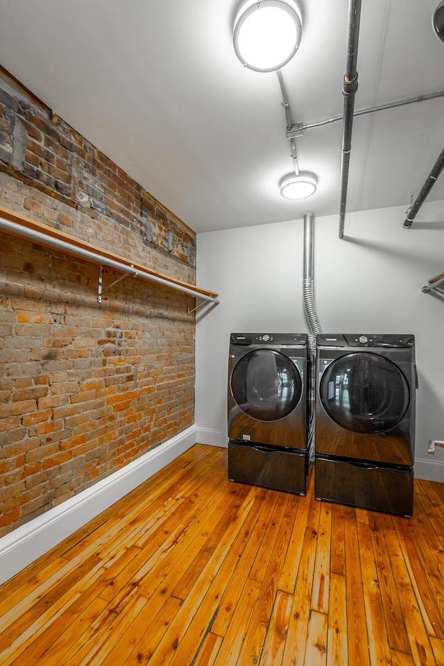 laundry area featuring brick wall, baseboards, wood-type flooring, and washing machine and clothes dryer