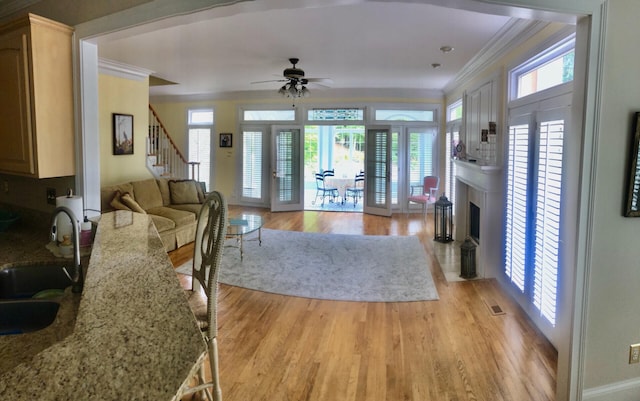 living room featuring light wood-type flooring, ceiling fan, ornamental molding, and sink