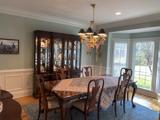 dining area with wood-type flooring, an inviting chandelier, and ornamental molding