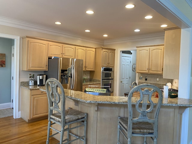 kitchen with light stone counters, kitchen peninsula, light hardwood / wood-style floors, light brown cabinetry, and appliances with stainless steel finishes