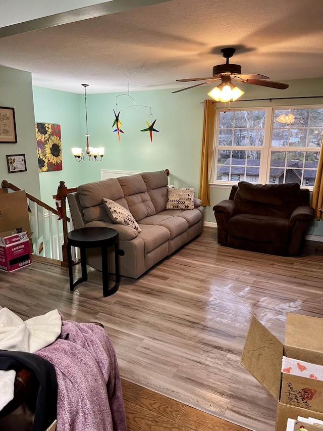 living room featuring ceiling fan with notable chandelier, a textured ceiling, and light wood-type flooring