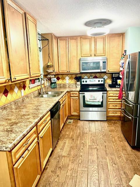 kitchen featuring sink, light wood-type flooring, a textured ceiling, tasteful backsplash, and stainless steel appliances