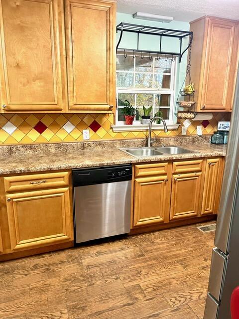 kitchen with sink, stainless steel dishwasher, light wood-type flooring, a textured ceiling, and tasteful backsplash