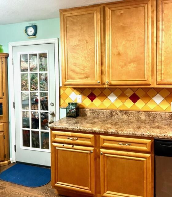 kitchen with decorative backsplash, hardwood / wood-style flooring, stainless steel dishwasher, and light stone counters