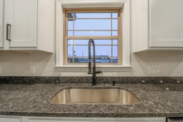 room details featuring white cabinets, sink, and dark stone counters