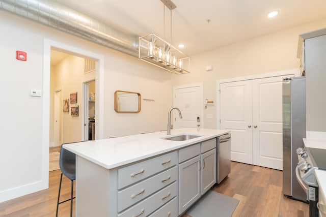 kitchen with gray cabinetry, a kitchen island with sink, sink, wood-type flooring, and hanging light fixtures