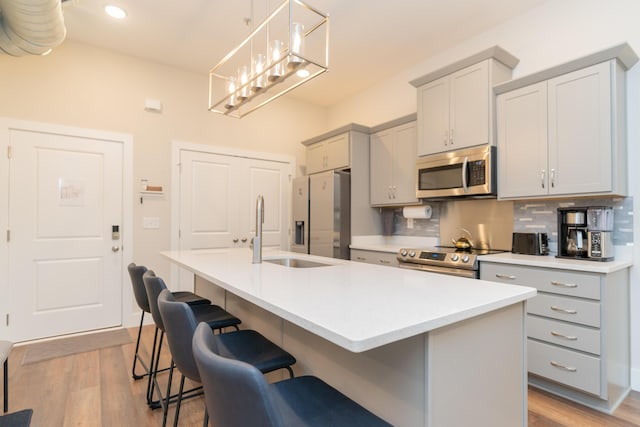 kitchen featuring sink, an island with sink, light wood-type flooring, and appliances with stainless steel finishes