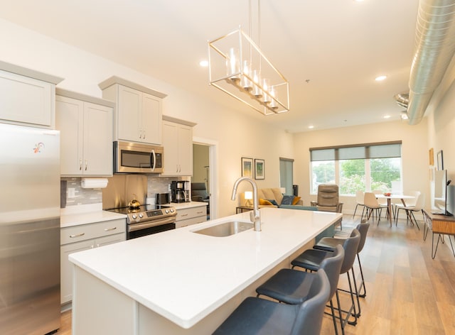 kitchen featuring stainless steel appliances, sink, decorative light fixtures, light hardwood / wood-style floors, and an island with sink