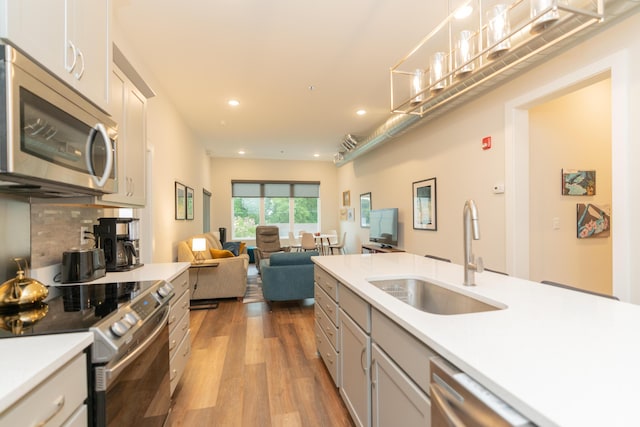 kitchen with stainless steel appliances, sink, white cabinets, light hardwood / wood-style floors, and hanging light fixtures