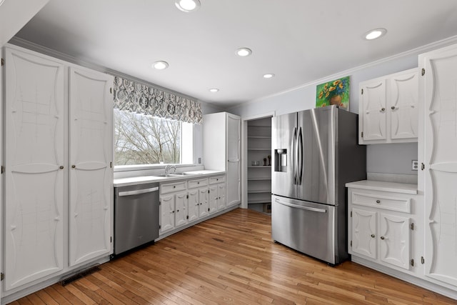 kitchen featuring stainless steel appliances, white cabinetry, light hardwood / wood-style floors, and crown molding