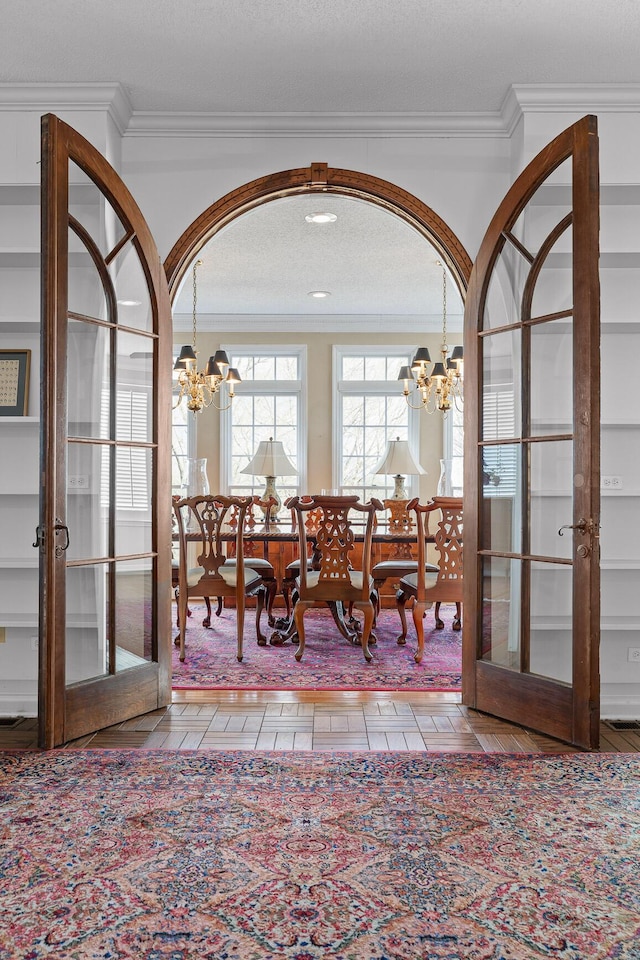 dining room with a textured ceiling, a notable chandelier, crown molding, and french doors