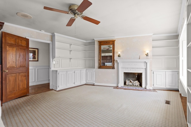 unfurnished living room featuring ceiling fan, built in features, crown molding, light carpet, and a fireplace