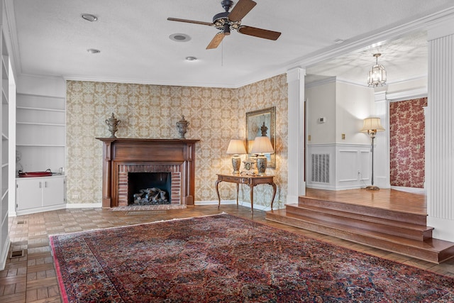 living room with built in shelves, parquet flooring, crown molding, a fireplace, and ceiling fan with notable chandelier