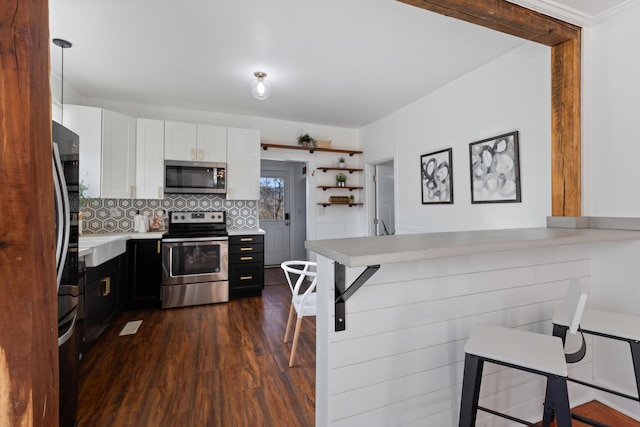 kitchen with decorative light fixtures, tasteful backsplash, white cabinetry, appliances with stainless steel finishes, and dark wood-type flooring