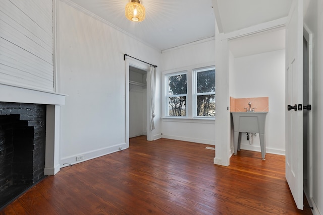 unfurnished bedroom with a closet, a fireplace, crown molding, and dark hardwood / wood-style floors