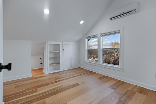 additional living space featuring lofted ceiling, a wall mounted AC, built in features, and light hardwood / wood-style flooring