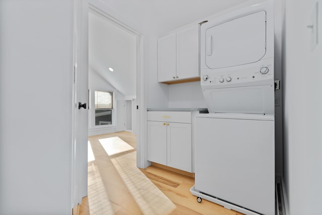 clothes washing area with cabinets, stacked washer and clothes dryer, and light hardwood / wood-style flooring