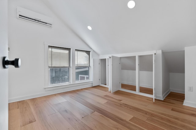 additional living space featuring lofted ceiling, an AC wall unit, and light hardwood / wood-style floors