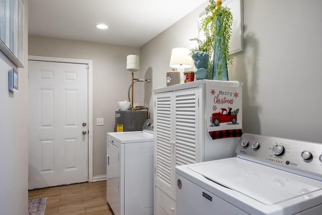 clothes washing area with washing machine and dryer, light hardwood / wood-style flooring, and water heater