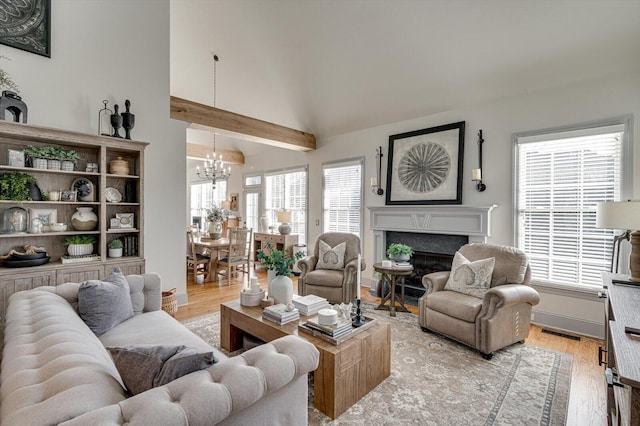 living room with a fireplace, lofted ceiling with beams, light hardwood / wood-style floors, and a chandelier