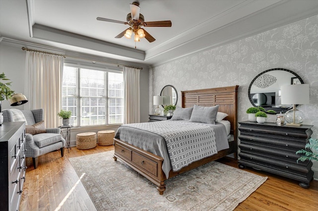 bedroom featuring a raised ceiling, ceiling fan, crown molding, and light wood-type flooring