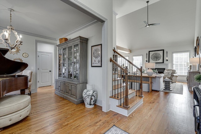 interior space featuring lofted ceiling, ornamental molding, ceiling fan with notable chandelier, and light wood-type flooring