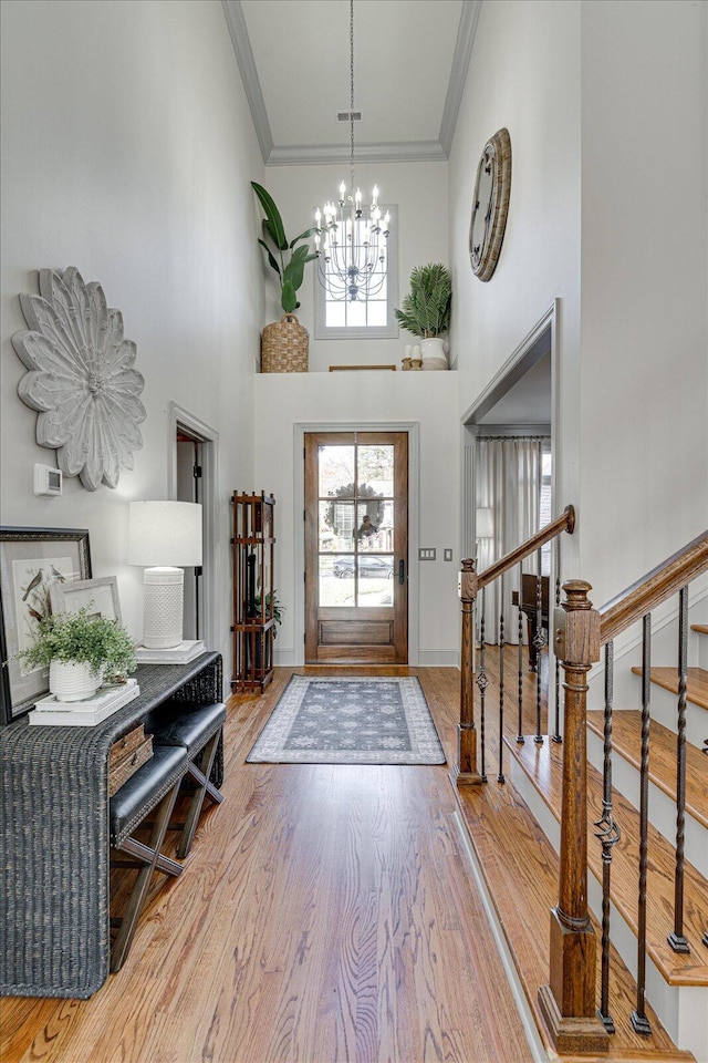 foyer entrance with an inviting chandelier, ornamental molding, a high ceiling, and hardwood / wood-style flooring