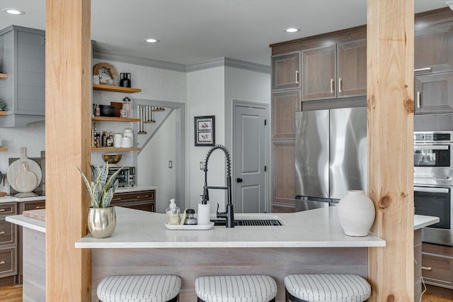 kitchen with stainless steel appliances, ornamental molding, kitchen peninsula, a breakfast bar, and hardwood / wood-style flooring