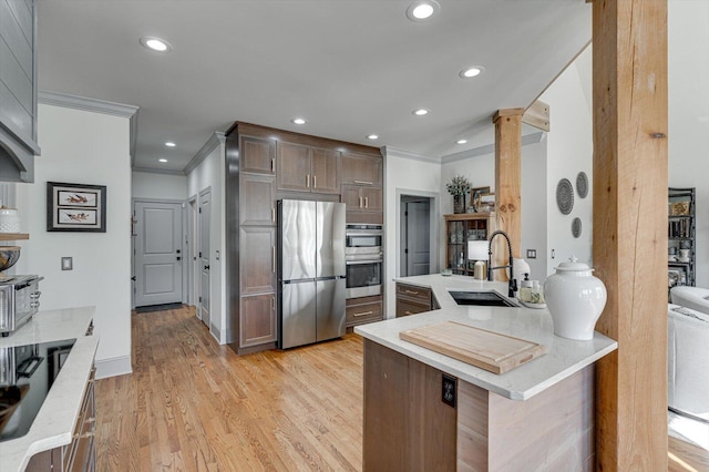 kitchen featuring ornate columns, sink, kitchen peninsula, light hardwood / wood-style floors, and appliances with stainless steel finishes