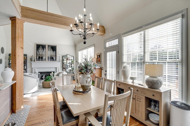 dining room featuring light wood-type flooring, lofted ceiling, a tile fireplace, and a chandelier