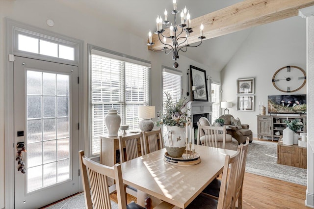 dining room featuring vaulted ceiling with beams, light hardwood / wood-style flooring, an inviting chandelier, and a brick fireplace