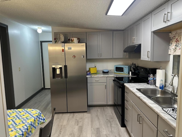 kitchen with a textured ceiling, stainless steel appliances, vaulted ceiling, and light hardwood / wood-style floors