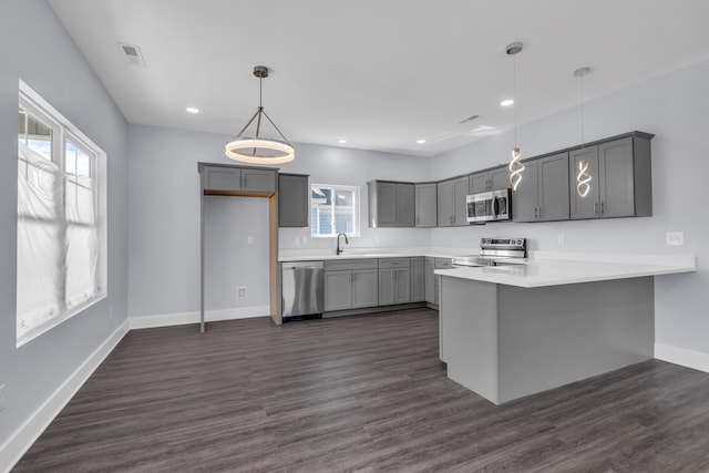 kitchen with sink, gray cabinets, appliances with stainless steel finishes, hanging light fixtures, and kitchen peninsula