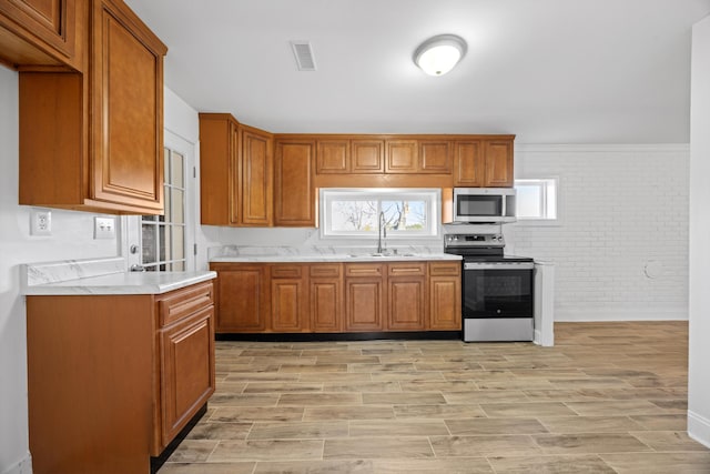 kitchen featuring brick wall, light wood-type flooring, sink, and appliances with stainless steel finishes