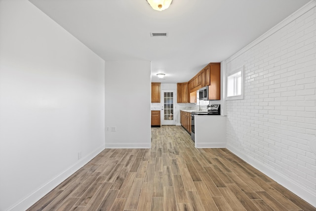 kitchen with light wood-type flooring, stainless steel appliances, and brick wall