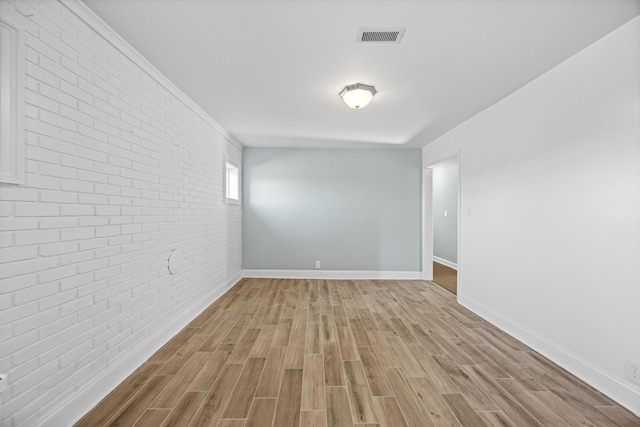 empty room featuring brick wall and light hardwood / wood-style floors