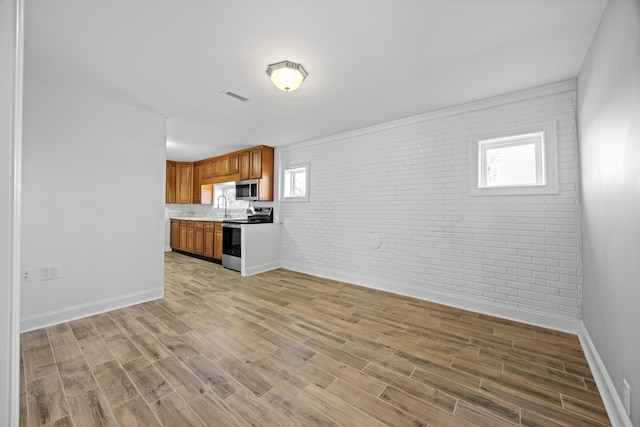 unfurnished living room featuring a healthy amount of sunlight, light wood-type flooring, sink, and brick wall