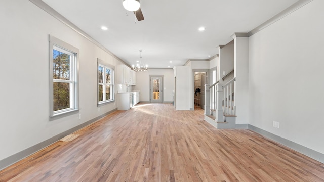 unfurnished living room featuring crown molding, ceiling fan with notable chandelier, and light hardwood / wood-style floors