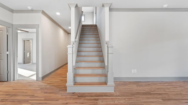 staircase with wood-type flooring, ornamental molding, and ceiling fan