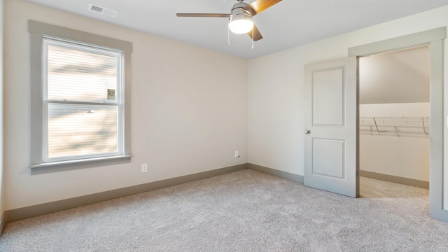 unfurnished bedroom featuring a spacious closet, light colored carpet, ceiling fan, and a closet