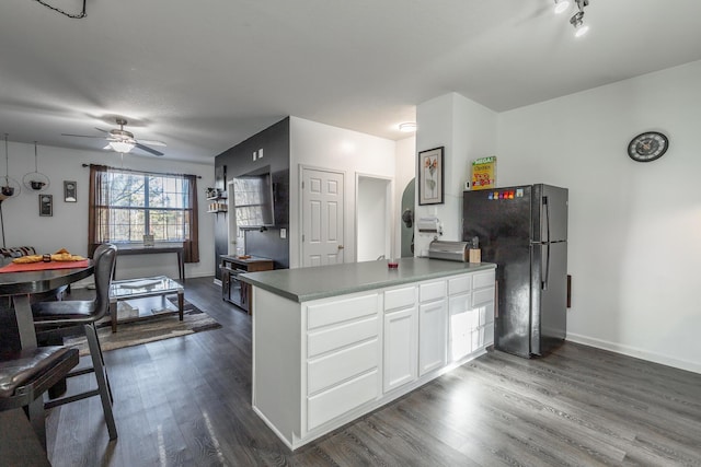 kitchen with kitchen peninsula, black fridge, ceiling fan, white cabinets, and dark hardwood / wood-style floors