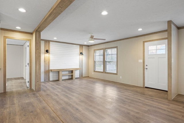 unfurnished living room featuring ceiling fan, ornamental molding, a textured ceiling, and light wood-type flooring