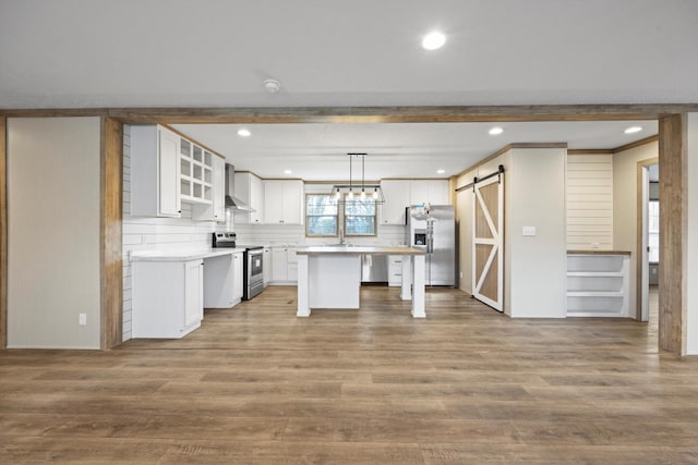 kitchen with a kitchen island, a barn door, decorative light fixtures, white cabinets, and appliances with stainless steel finishes