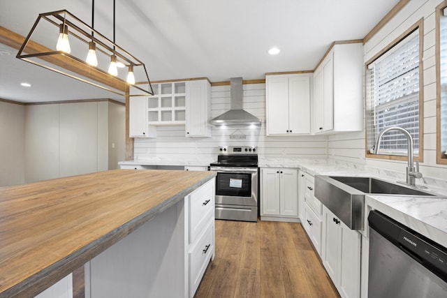 kitchen with white cabinetry, wall chimney exhaust hood, decorative light fixtures, and appliances with stainless steel finishes