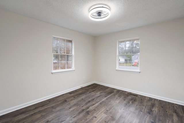 empty room featuring a textured ceiling, a healthy amount of sunlight, and dark wood-type flooring